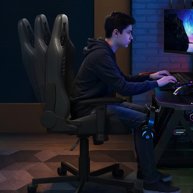 Person sitting on a gaming chair in front of a computer setup in a dimly lit room.
