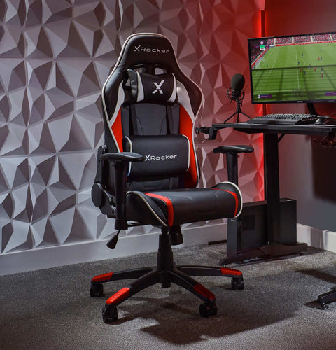 Gaming chair with X rocker branding in a room with a geometric wall design and computer setup.