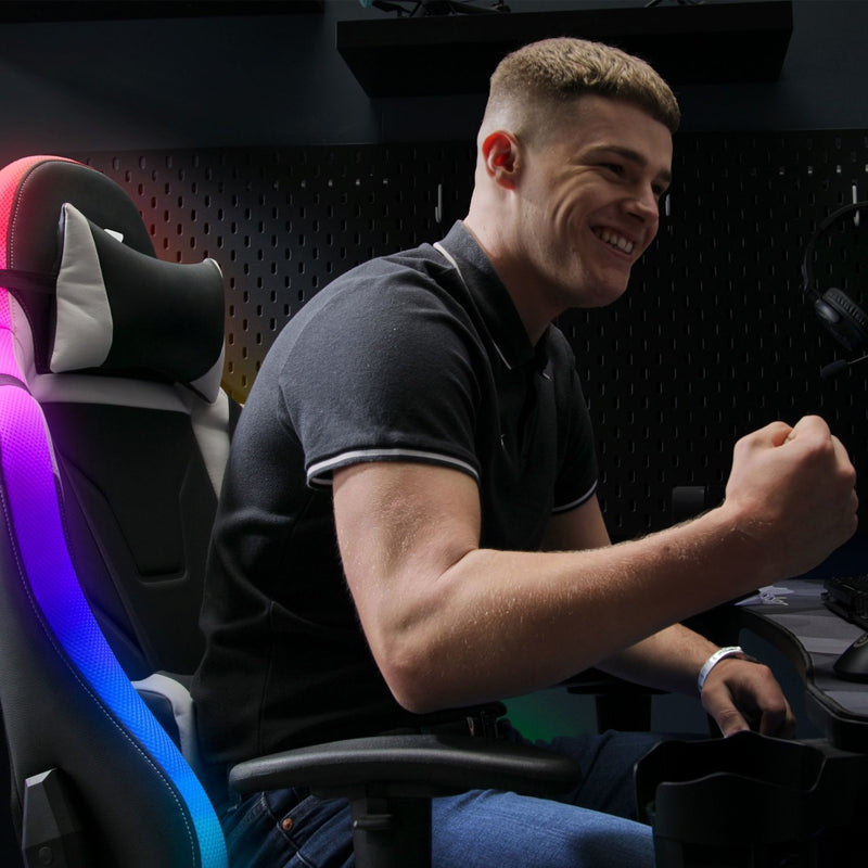 Man sitting in a gaming chair with colorful lighting, smiling.