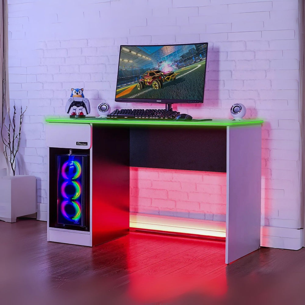 Gaming desk with RGB lighting, computer setup, and colorful monitor in a room with white brick walls.