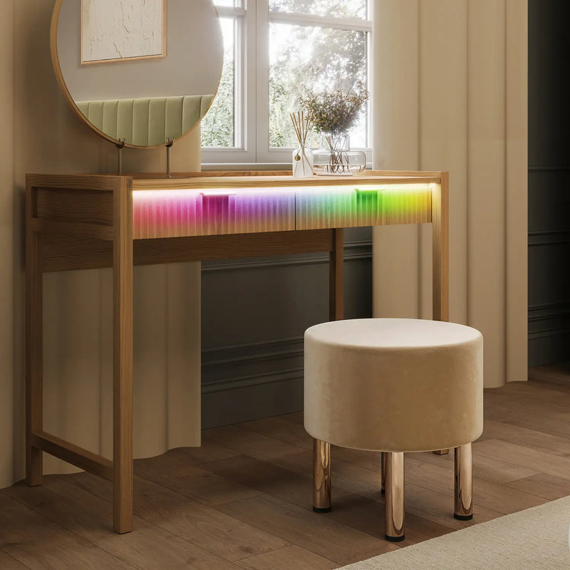 Wooden vanity table with colorful LED strip lighting and a round stool in a room with a window and curtains.