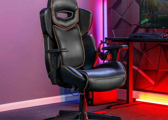 Gaming chair in a room with a desk and computer setup, featuring colorful lighting.