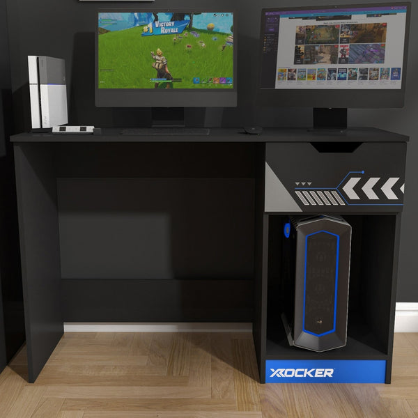 Gaming setup with two monitors, gaming console, and X-Rocker speaker on a black L-shaped desk.