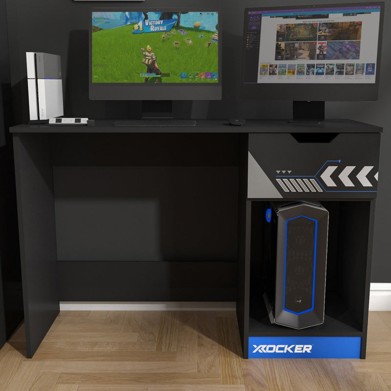 Gaming setup with two monitors, gaming console, and X-Rocker speaker on a black L-shaped desk.