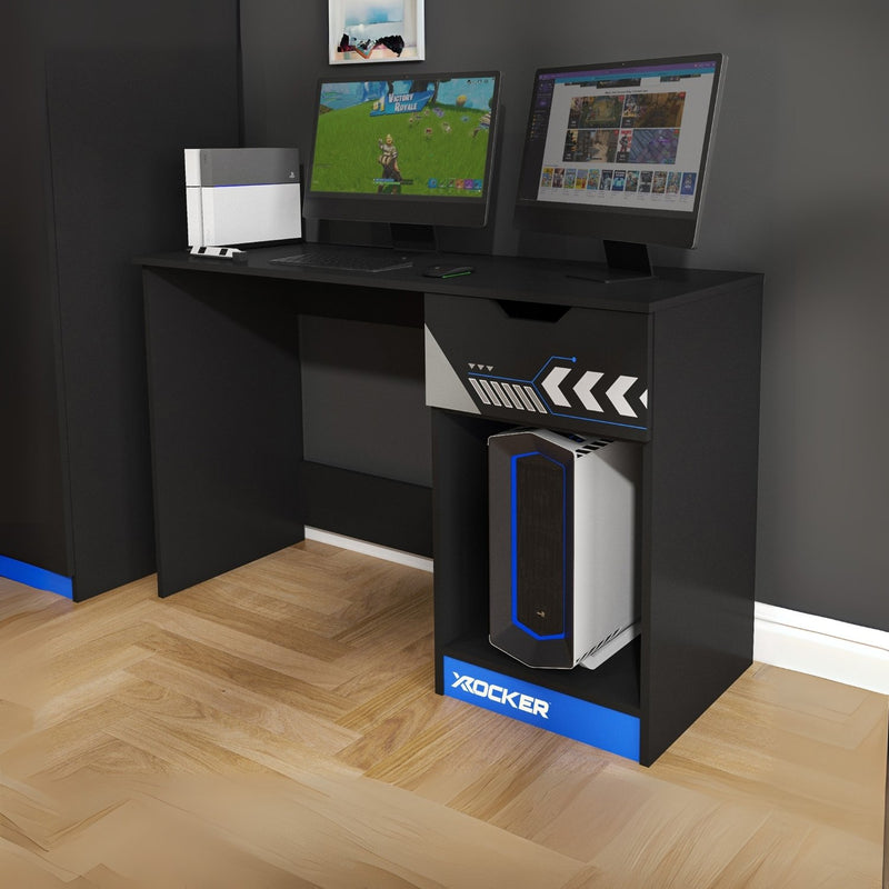 Black gaming desk with two monitors and a X rocker gaming chair on a wooden floor.
