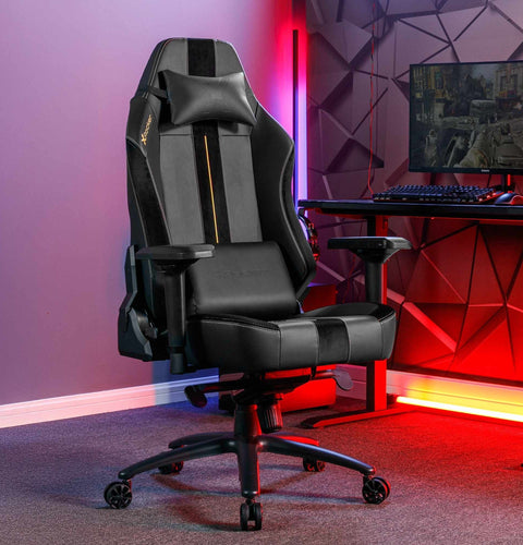 Gaming chair in a room with a desk and computer setup, illuminated by colorful lights.