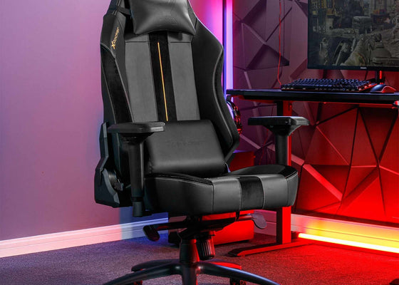 Gaming chair in a room with a desk and computer setup, illuminated by colorful lights.