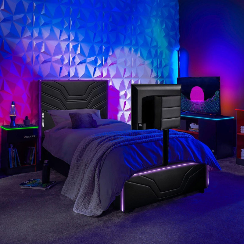 Modern gaming bedroom with a black bed and geometric wall design, illuminated by colorful lights with x rocker gaming furniture.