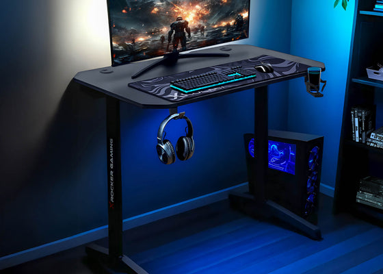 Gaming desk setup with monitor, keyboard, mouse, and headphones in a dark room.