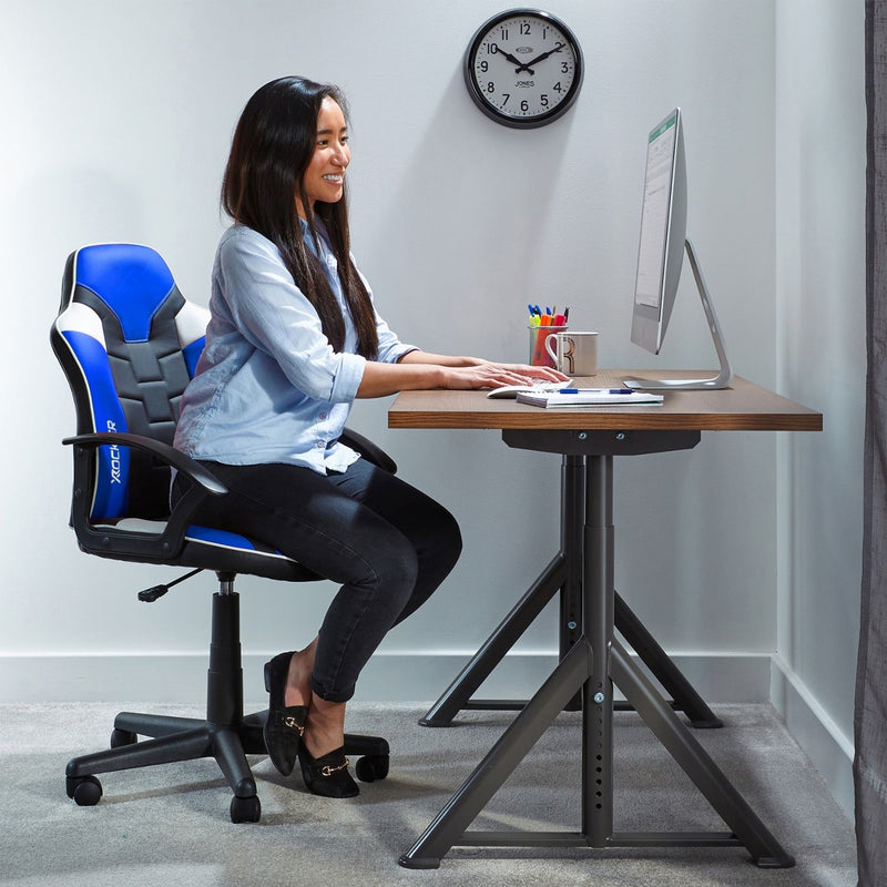 Woman sitting at a desk with a gaming chair, computer, and clock on the wall.