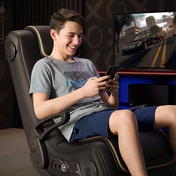 Person sitting in a gaming chair using a smartphone with a TV displaying a racing game in the background.