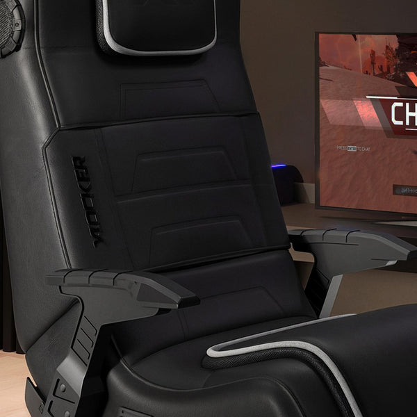 Black gaming chair with armrests in a room with a computer monitor displaying a game.