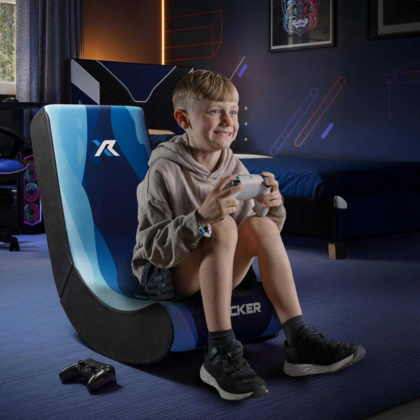 Child sitting on a blue and black gaming chair holding a controller in a room with gaming setup.