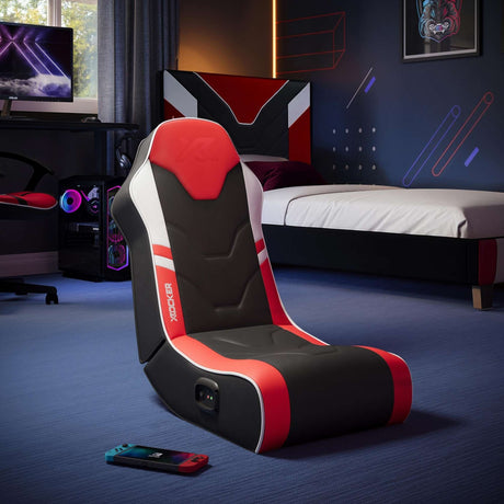 Gaming chair with red and black design in a room with gaming setup and bed.