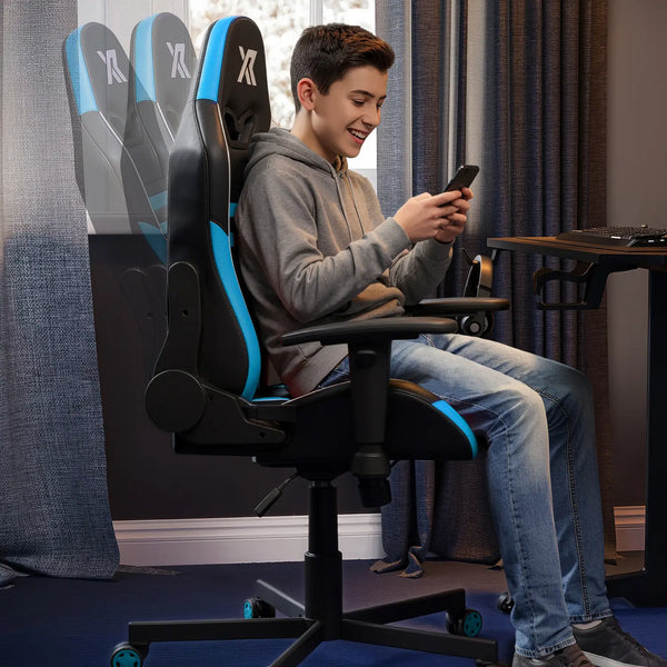 Person sitting on a gaming chair using a smartphone in a room with curtains and a desk.
