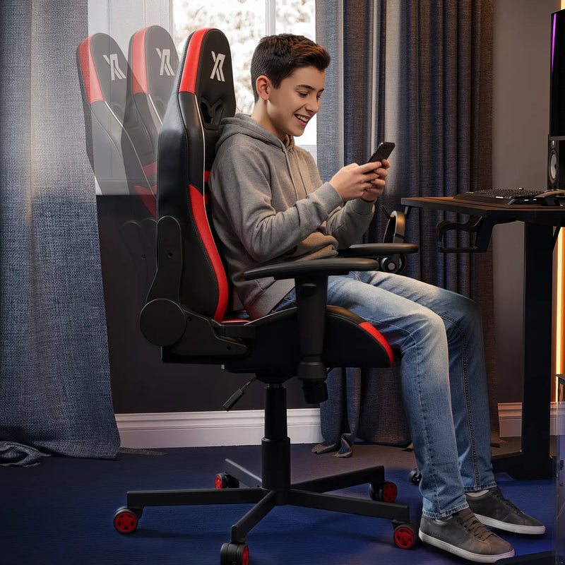 Person sitting on a black and red gaming chair in a room with a desk and computer setup.