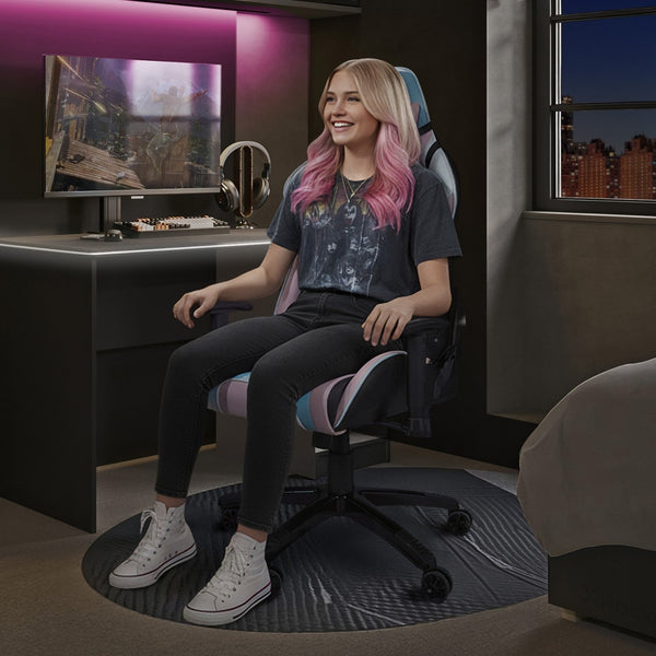 Woman with pink hair sitting in a gaming chair in a room with a desk and computer setup.