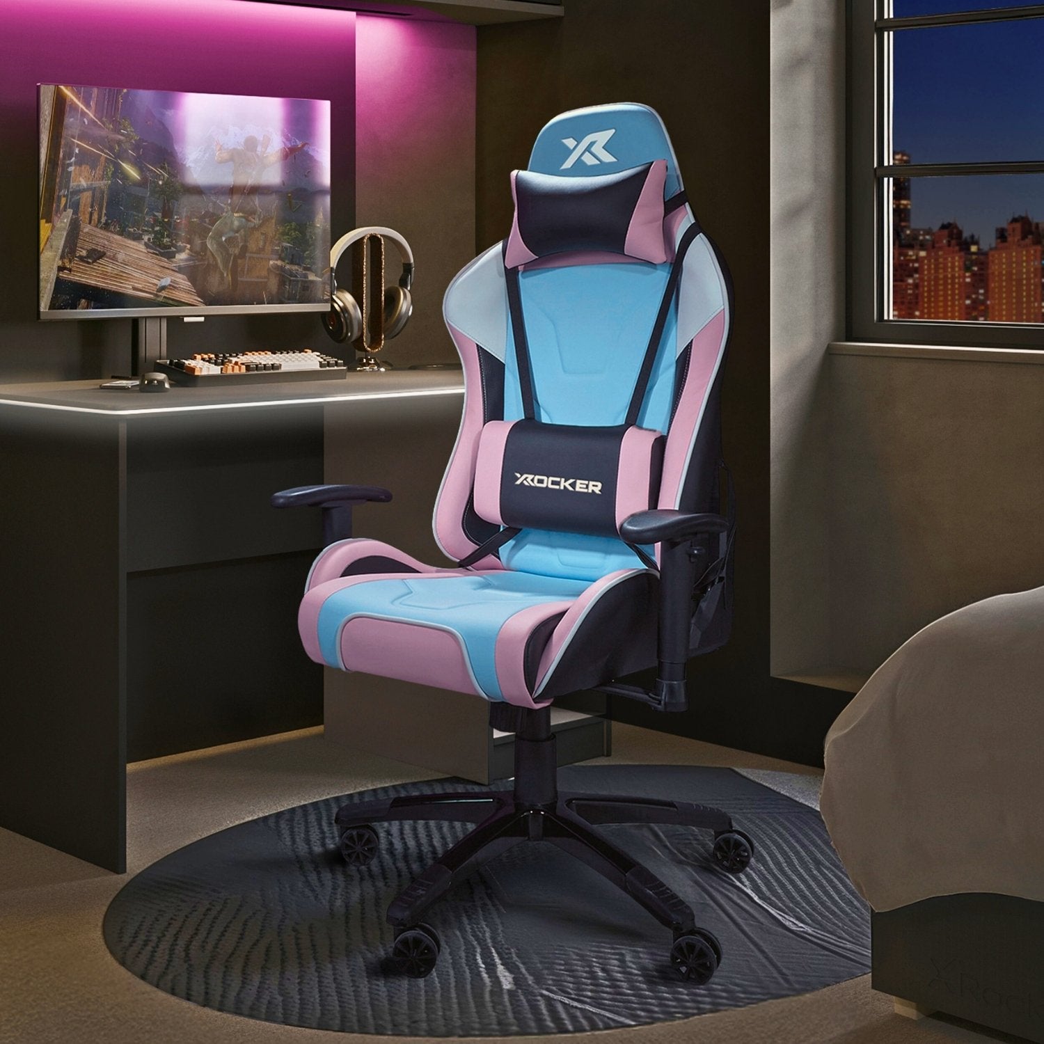 Gaming chair with pink and blue accents in a room with a desk and computer setup.