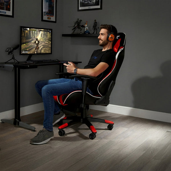 Man sitting in a gaming chair in a room with a desk and computer setup.