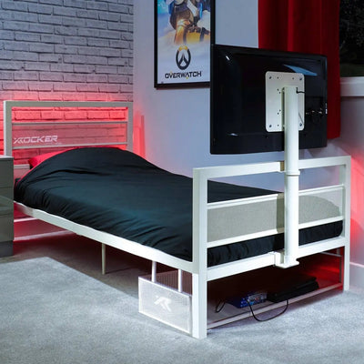 White metal tv bed frame with black mattress in a room with a TV and gaming decor.