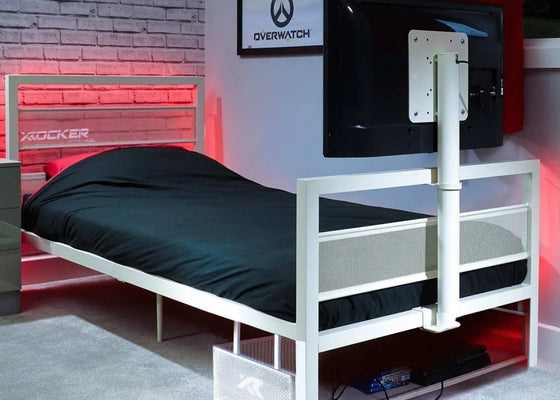 White metal tv bed frame with black mattress in a room with a TV and gaming decor.