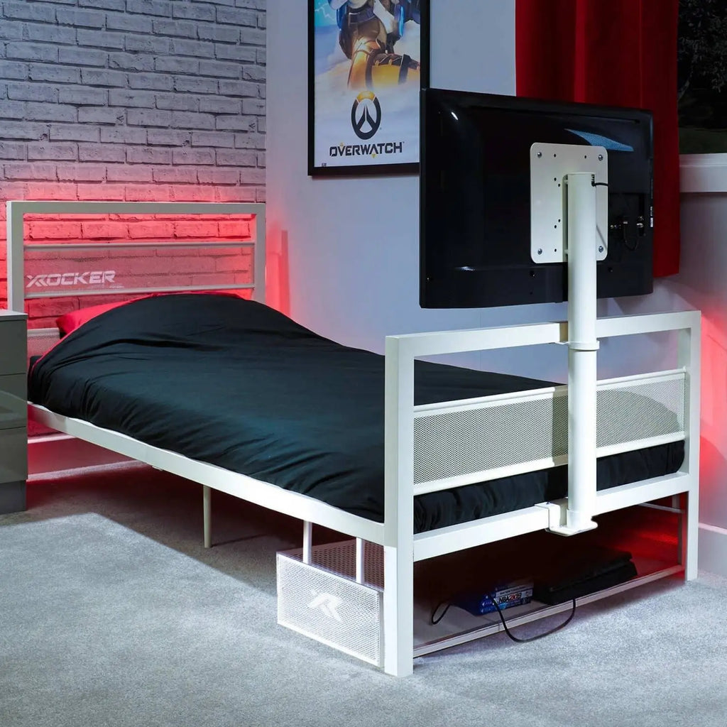 White metal tv bed frame with black mattress in a room with a TV and gaming decor.