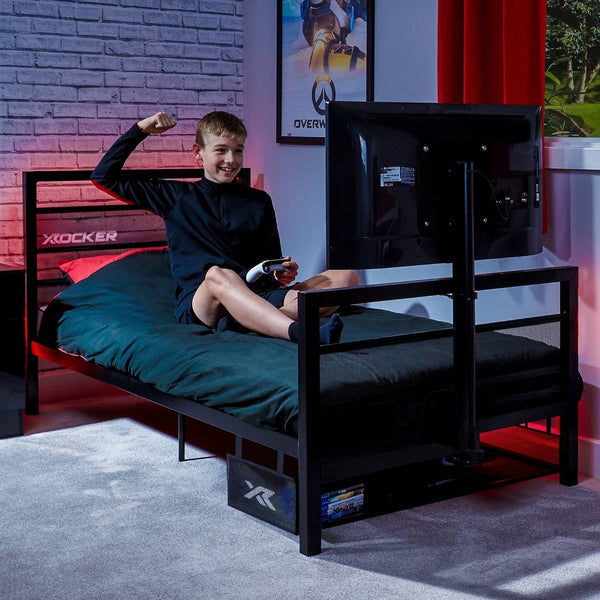 Child sitting on a X rocker gaming bed in a room with a TV and colorful walls.