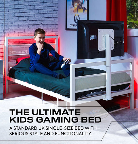 Child sitting on a gaming bed with a TV stand, surrounded by gaming equipment in a room with red and white decor.