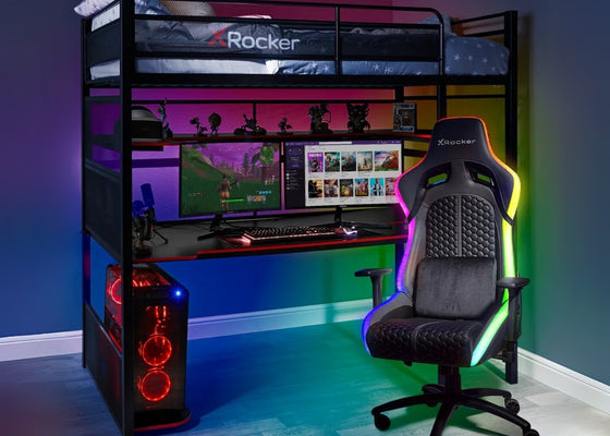 Gaming room setup with a desk, chair, and computer equipment in a room with colorful lighting.