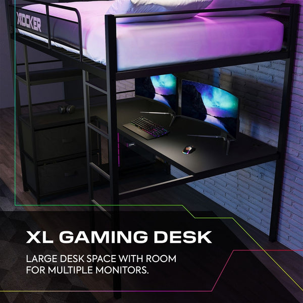Gaming desk with computer setup under a loft bed in a room with brick walls.