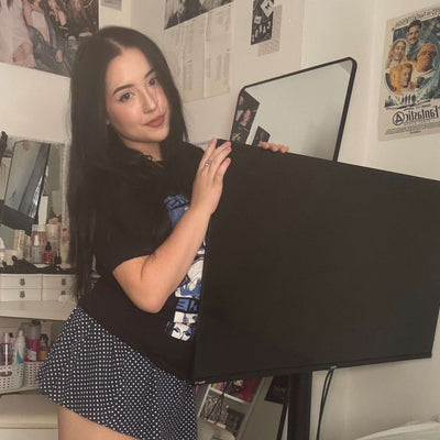 Woman standing by a black screen in a room with posters on the wall