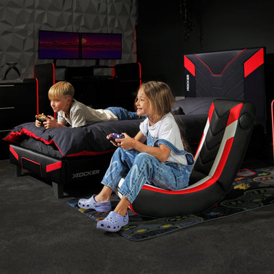 Two children playing video games on a gaming chair and the cerberus bed in a dark room