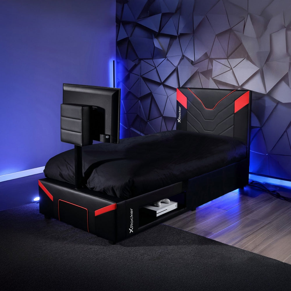 Gaming bed setup with monitor and gaming chair in a room with geometric wall design.