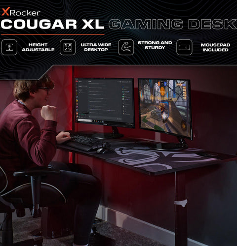 X rocker Cougar XL gaming desk with a person using it, featuring height adjustable, ultra wide desktop, and mousepad included.