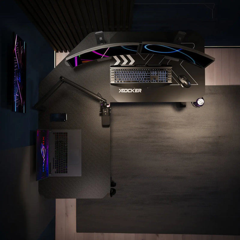 Dark gaming desk with X rocker brand name, computer setup, and illuminated elements.