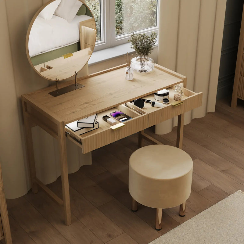 Wooden vanity table with round mirror and stool in a room with a window and curtains.