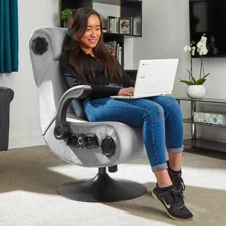 Woman using a laptop on a modern gaming chair in a living room setting.
