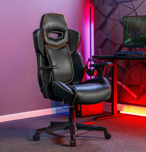 Gaming chair in a room with a desk and computer setup, featuring colorful lighting.