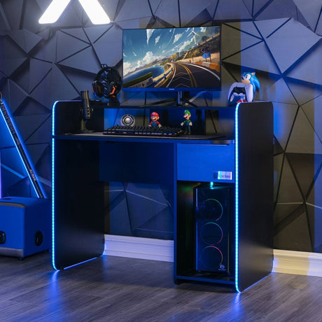 Gaming setup with a desk, computer monitor, and RGB lighting in a room with geometric wall design.