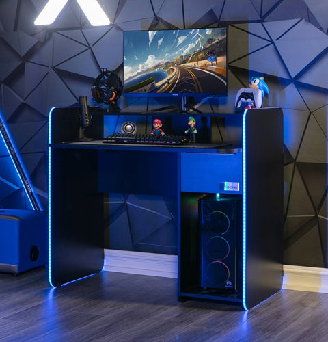 Gaming setup with a desk, computer monitor, and RGB lighting in a room with geometric wall design.