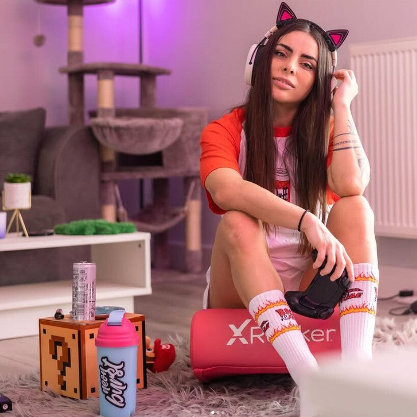 Woman sitting on a pink cushion with gaming accessories in a room.
