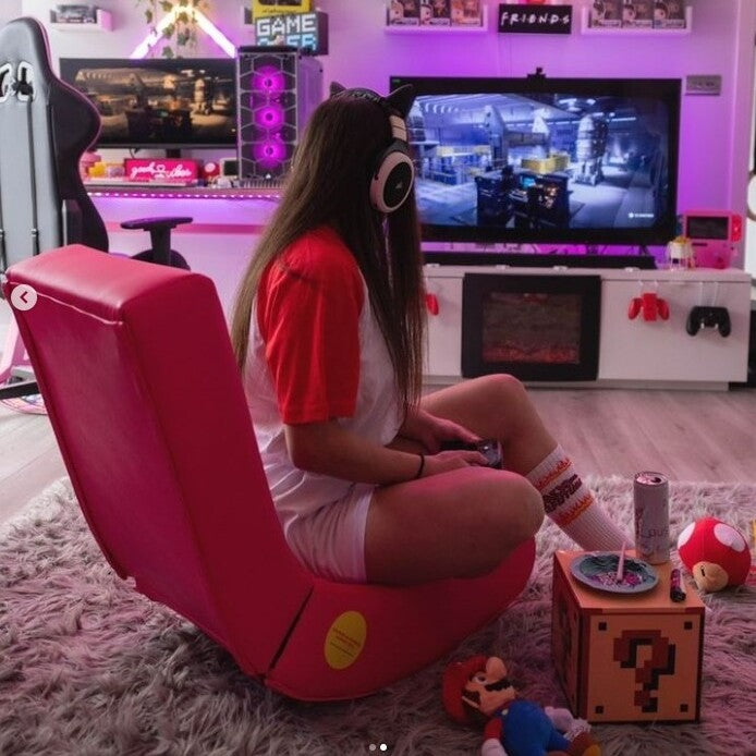 Person sitting on a pink gaming chair in a room with gaming setup and decor.