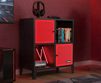 Black and red cube shelf with books and a gaming console in a room with red walls.
