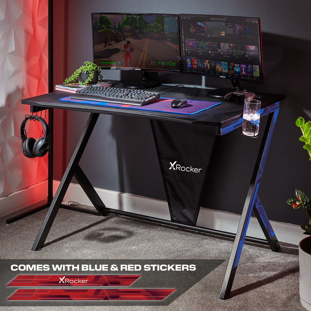 Gaming desk with X rocker branding, two monitors, keyboard, and mouse in a room setting.