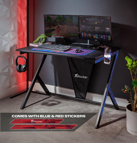 Gaming desk setup with multiple monitors, keyboard, mouse, and X rocker branding.