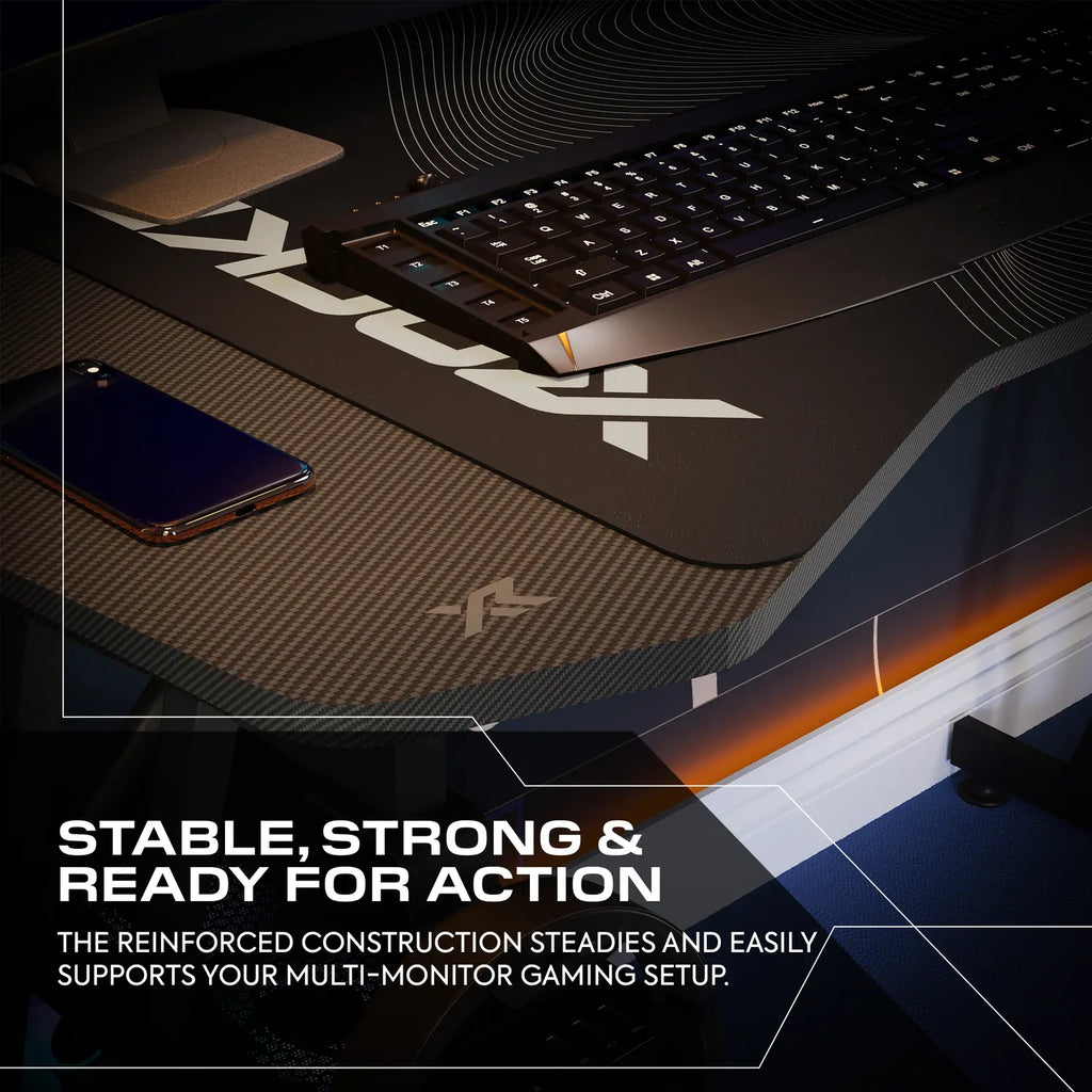 Gaming desk setup with monitor stand, keyboard, and phone on a dark surface.