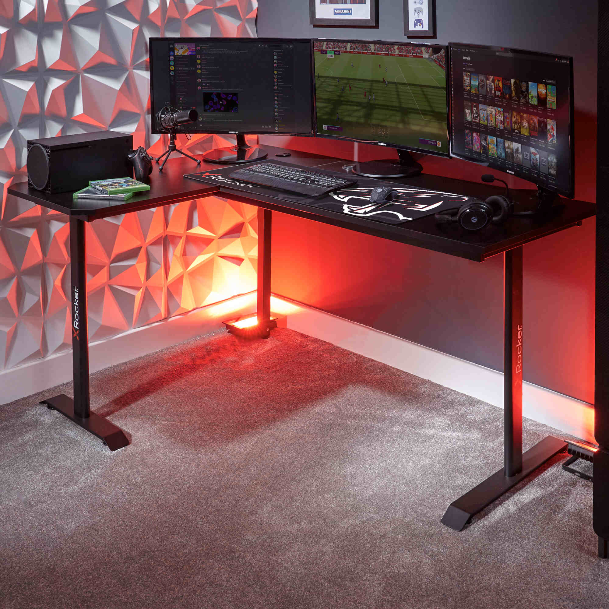 Gaming desk with multiple monitors and gaming equipment against a geometric wall.