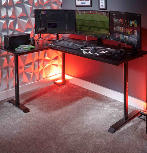 Gaming desk with multiple monitors and gaming equipment against a geometric wall.