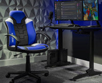 Gaming setup with a blue and black chair, desk, and dual monitors in a room with geometric wall design.