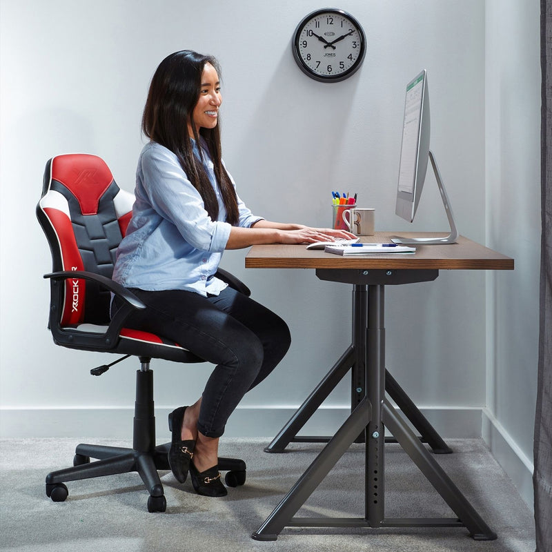 Woman sitting at a desk with a gaming chair, working on a computer.